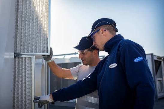 Two technicians inspecting a rooftop HVAC unit